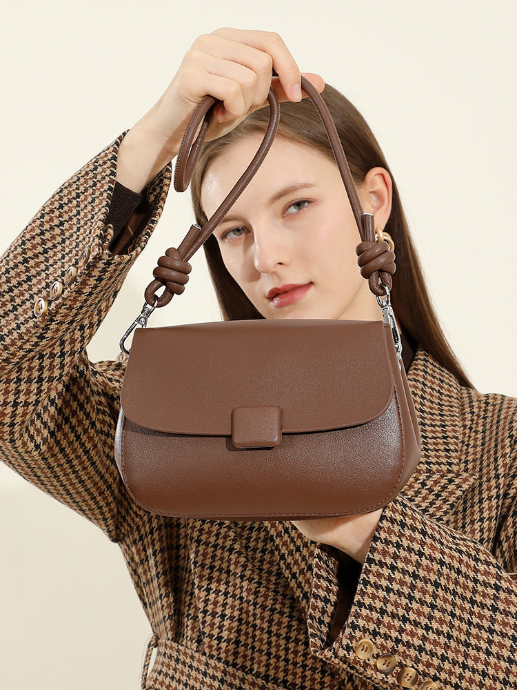 Model holding brown leather crossbody bag by knotted strap in houndstooth coat