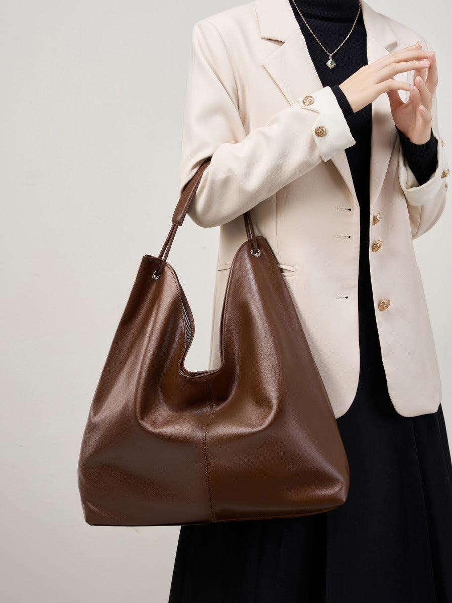 Brown hobo tote bag held in front with a beige blazer and black dress