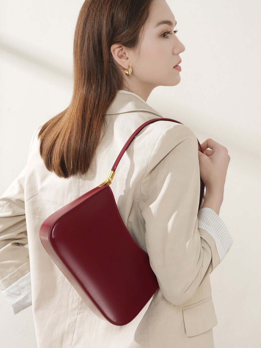 Wine red shoulder bag styled as an underarm bag on a model in a cream blazer