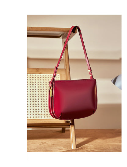Burgundy leather underarm bag hanging from a wooden rattan chair