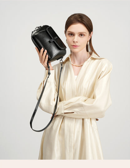 Model holding a black leather crossbody bag with silver-tone hardware