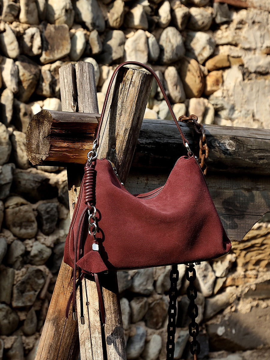 Wine purple nubuck shoulder bag hanging on wooden post outdoors