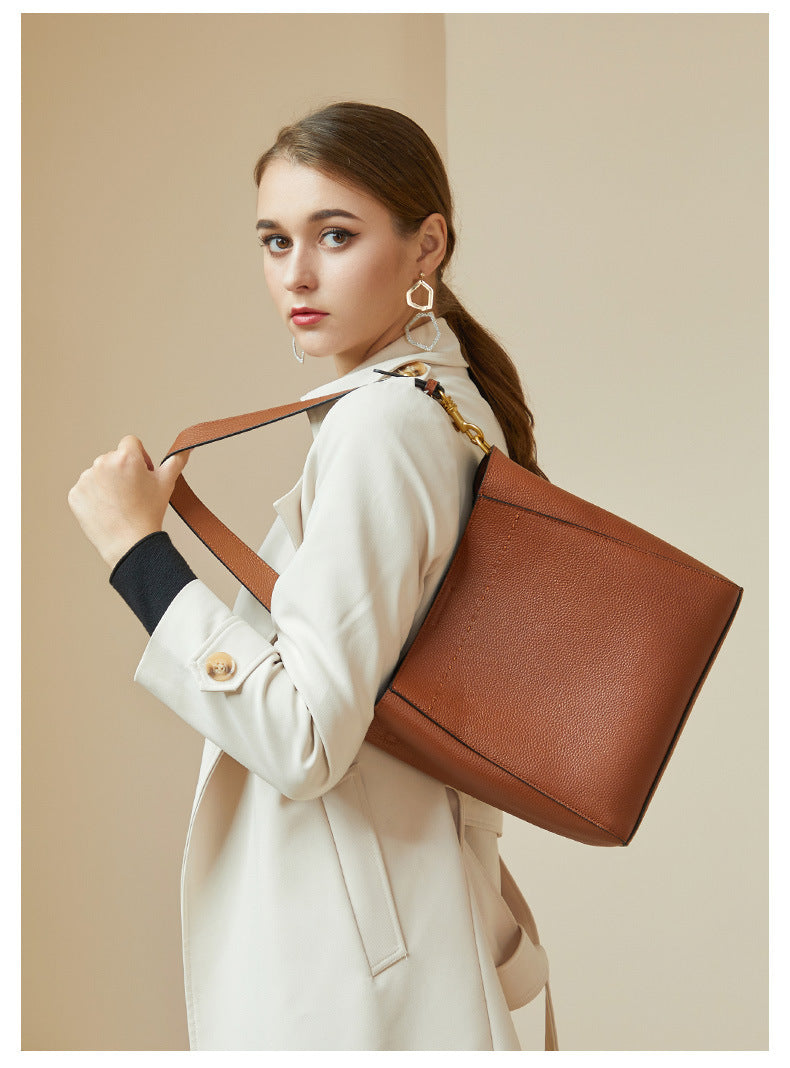 Model in cream coat with tan bucket bag tucked under arm showing back pocket
