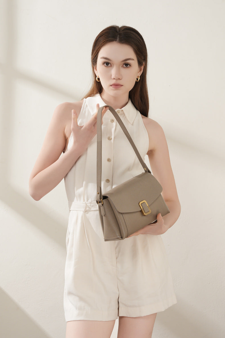 Model holding gray cowhide leather crossbody bag in hand with cream outfit
