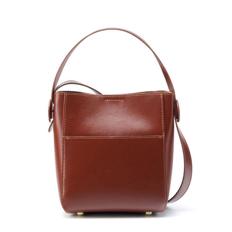 Brown cowhide leather bucket crossbody bag with top handle and shoulder strap on white background