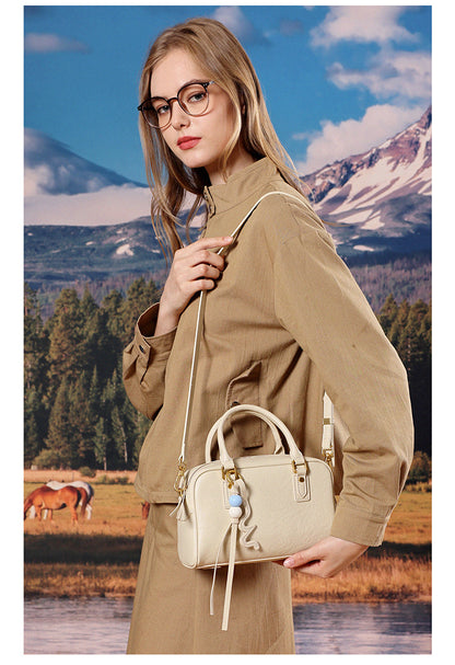 Model in tan outerwear carrying a cream leather pillow crossbody bag on her shoulder