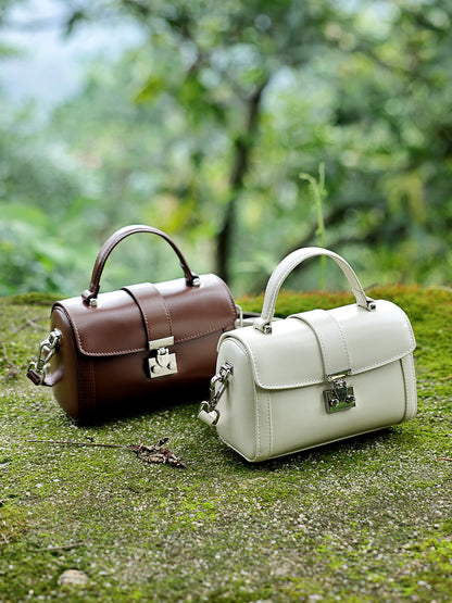 Brown and off-white cowhide leather mini box bags displayed side by side on moss