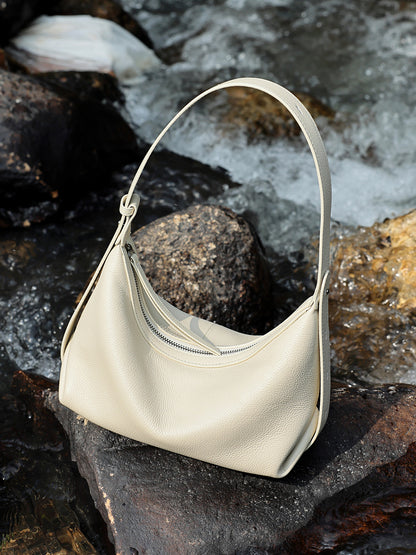 Ivory white hobo bag resting on rocks near water