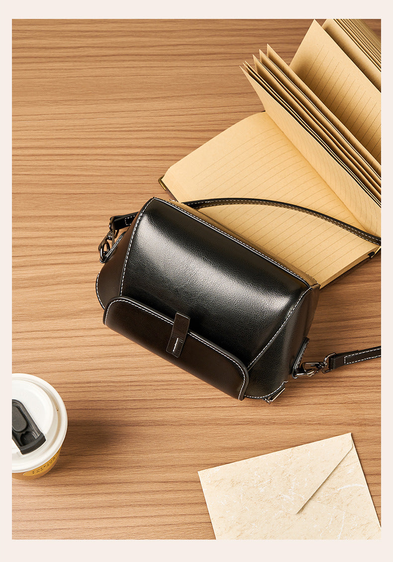 Top-down flat lay of black crossbody bag with open notebook and coffee cup