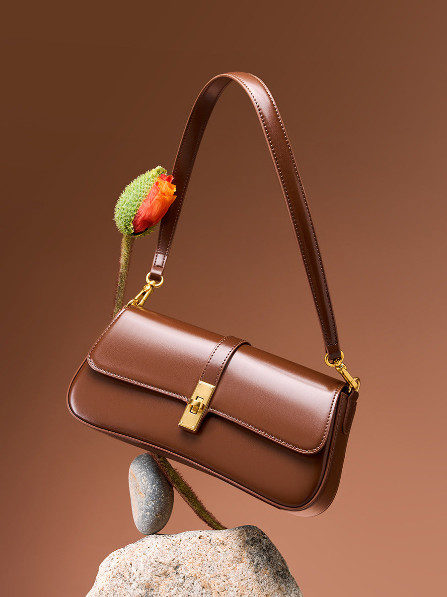 Stylized product shot of brown cowhide leather baguette bag with turn-lock closure on a stone pedestal