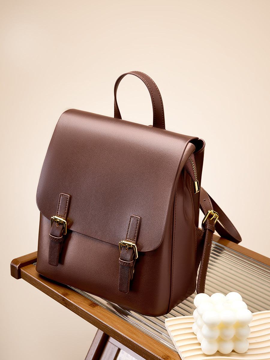 Dark brown leather backpack sitting on a glass-top wooden shelf with a candle in the foreground