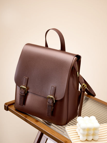 Dark brown leather backpack sitting on a glass-top wooden shelf with a candle in the foreground