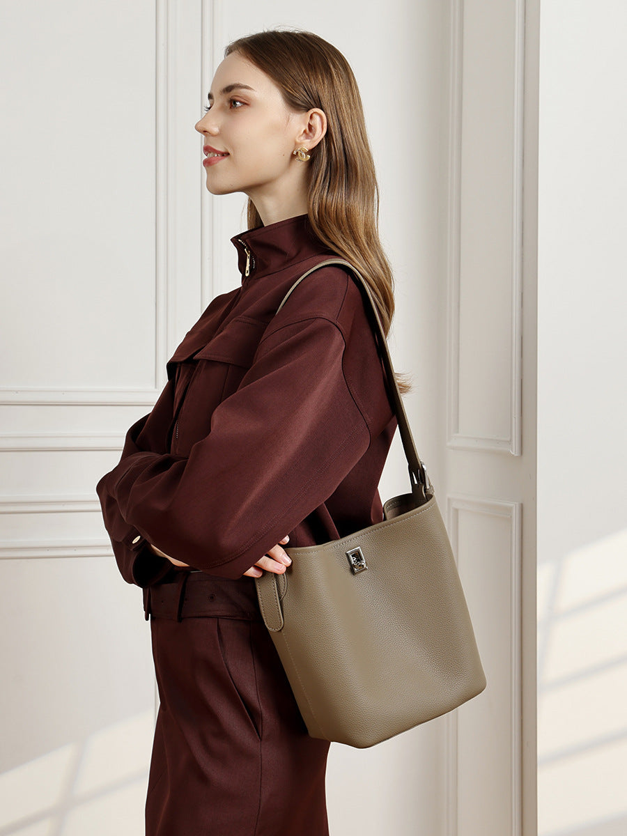 Model wearing khaki leather bucket bag as a shoulder bag with a dark brown jacket