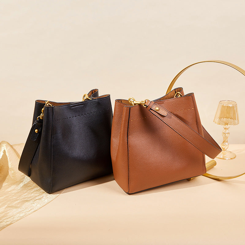 Black and tan cowhide leather bucket bags displayed side by side on neutral surface