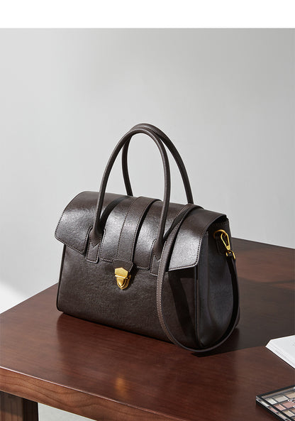 Dark brown leather satchel bag with top handles and shoulder strap on table