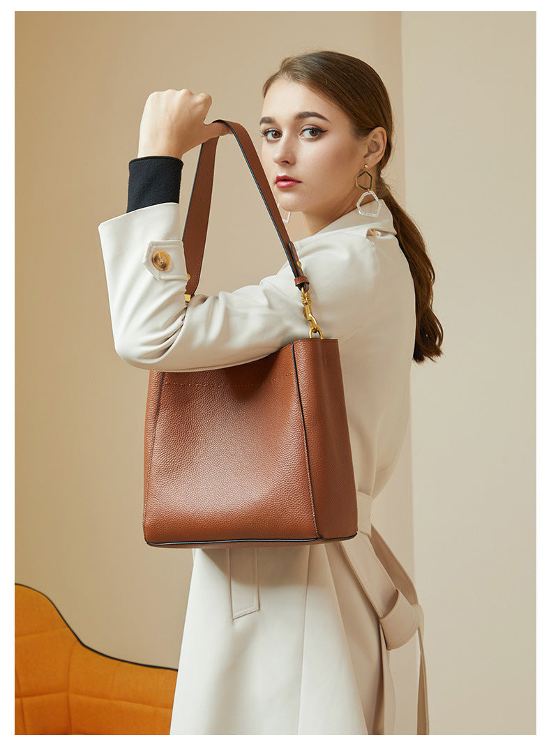 Model with ponytail carrying tan bucket bag in hand showing removable strap