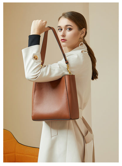 Model with ponytail carrying tan bucket bag in hand showing removable strap