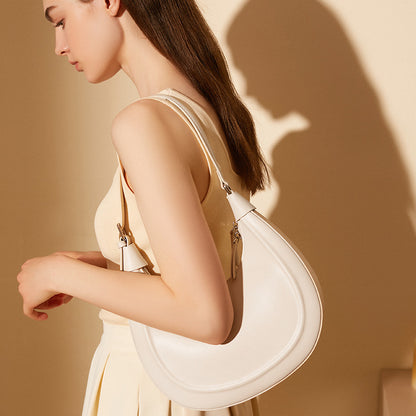 Side view of a cream white crescent cowhide shoulder bag styled under the arm