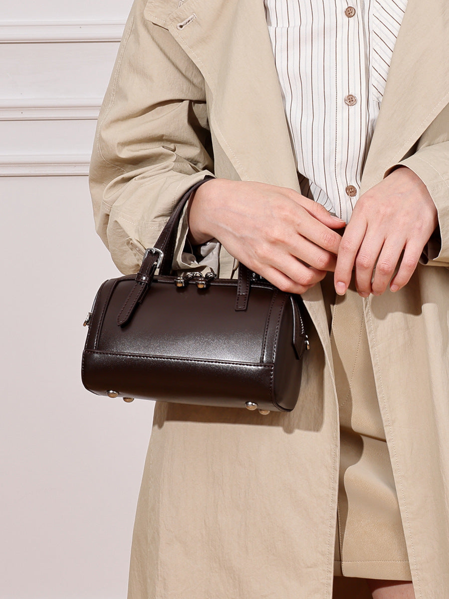 Brown cowhide leather mini Boston bowling bag carried by hand in trench coat styling