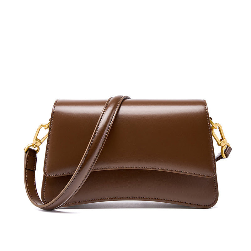 Three-quarter view of brown cowhide leather baguette bag with flap and adjustable straps