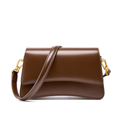 Three-quarter view of brown cowhide leather baguette bag with flap and adjustable straps
