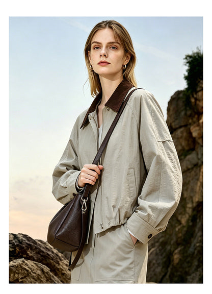 Front view of a model in a light jacket wearing a coffee brown crossbody bag with adjustable strap