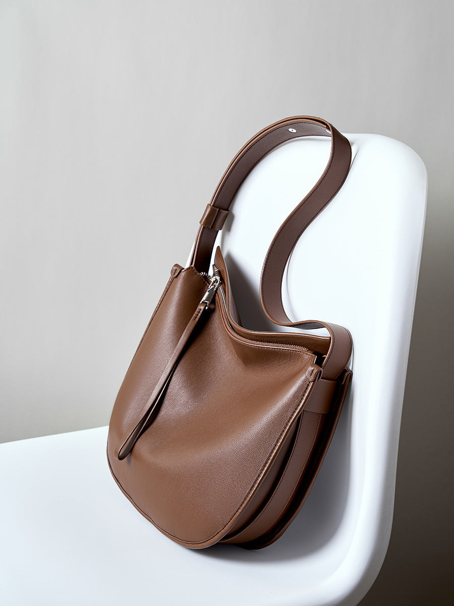 Brown leather hobo bag displayed on white chair showing adjustable strap