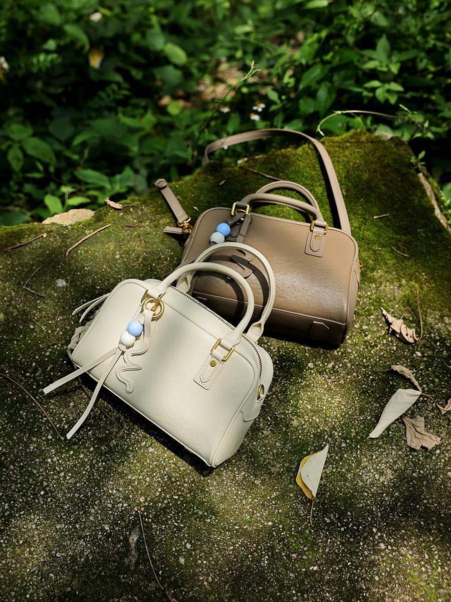 Two cowhide leather pillow bags in cream and taupe resting on a mossy rock