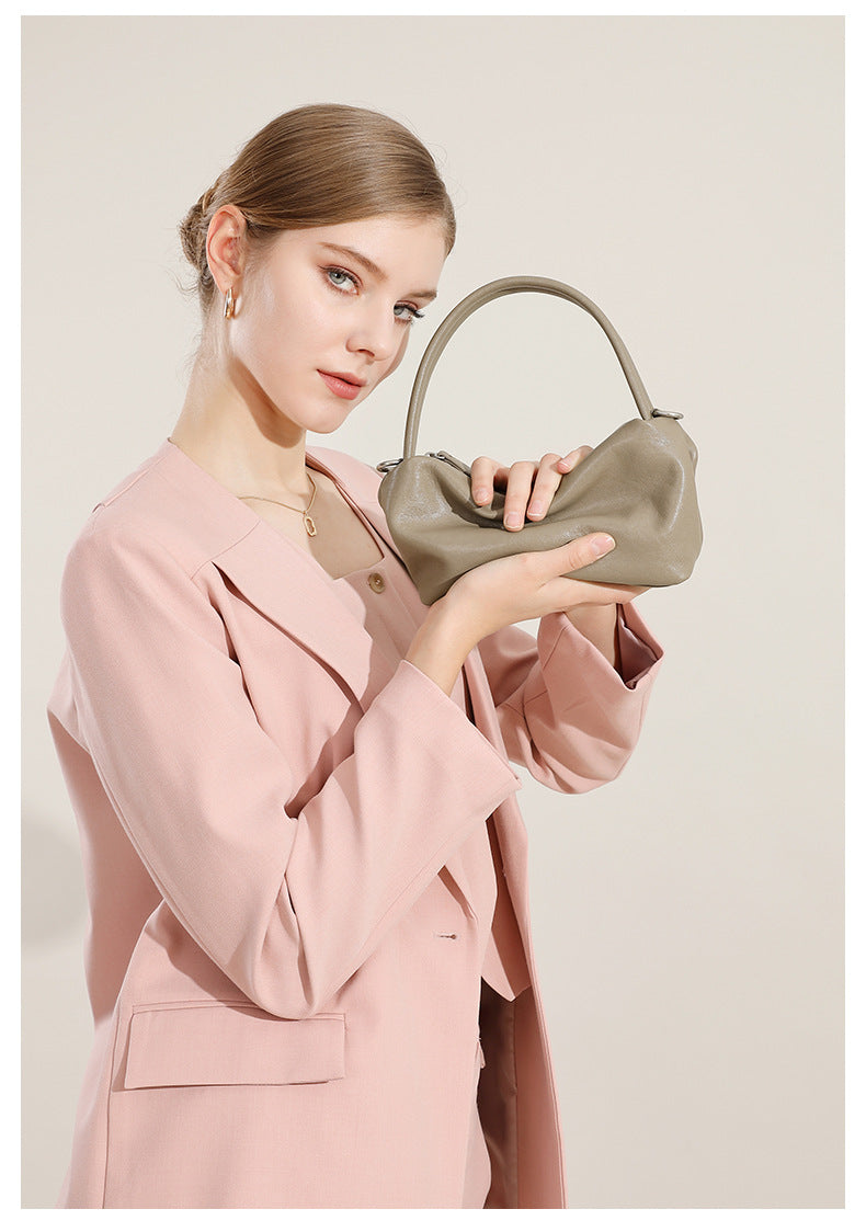 Gray pillow bag held in hands by a model in a pink blazer