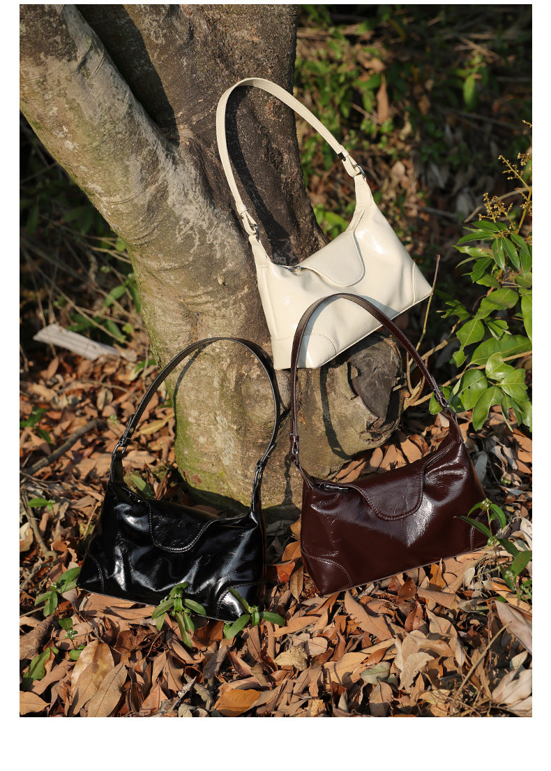 Black, coffee, and pearl white leather shoulder bags arranged on a forest floor
