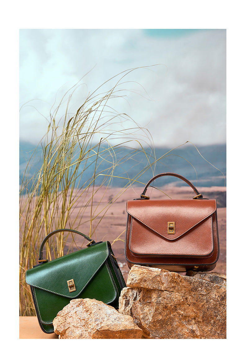 Brown and green leather messenger bags on rocks with tall grass and mountain view