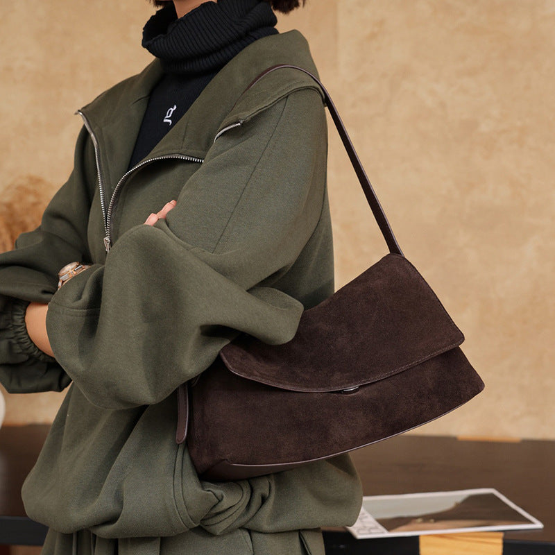 Side view of a brown leather shoulder bag worn with a jacket
