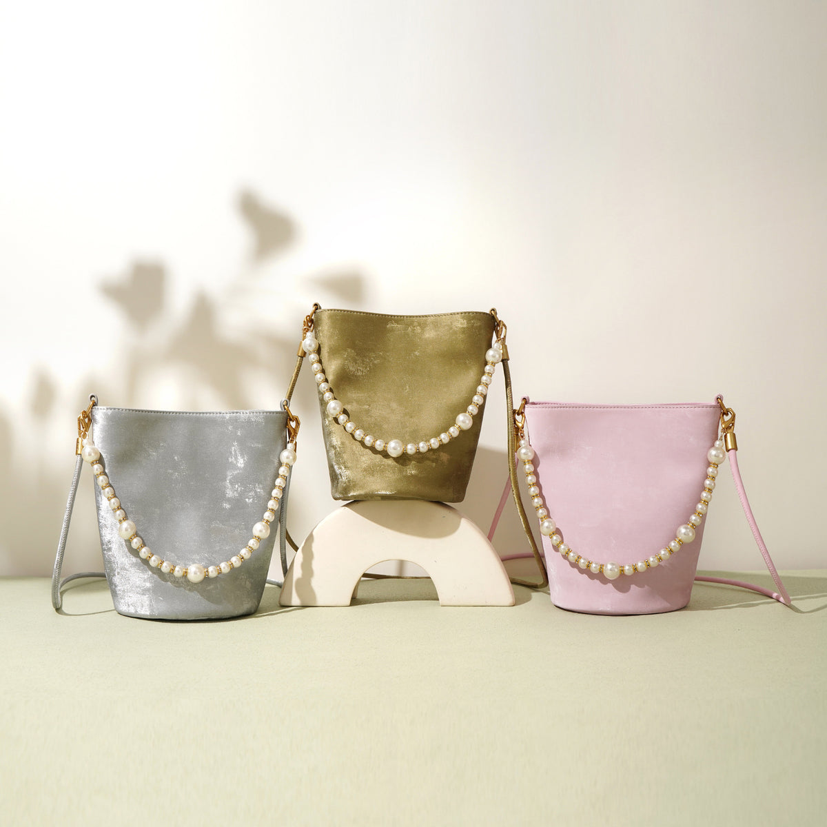 Three mini bucket bags in moss green, silver gray, and blush pink arranged on a table