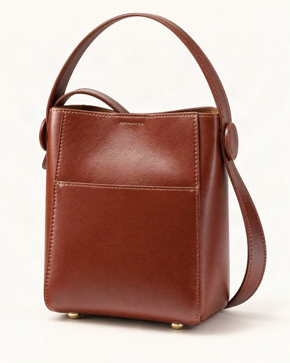 Cowhide Leather Bucket Crossbody Bag — front three-quarter view on a warm white background